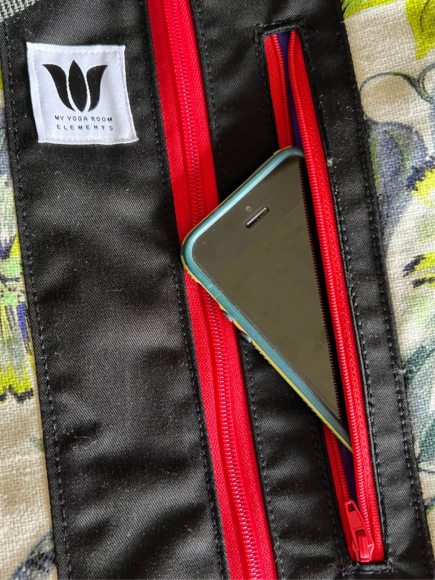Phone in a red-zippered pouch with a visible brand label on a floral background