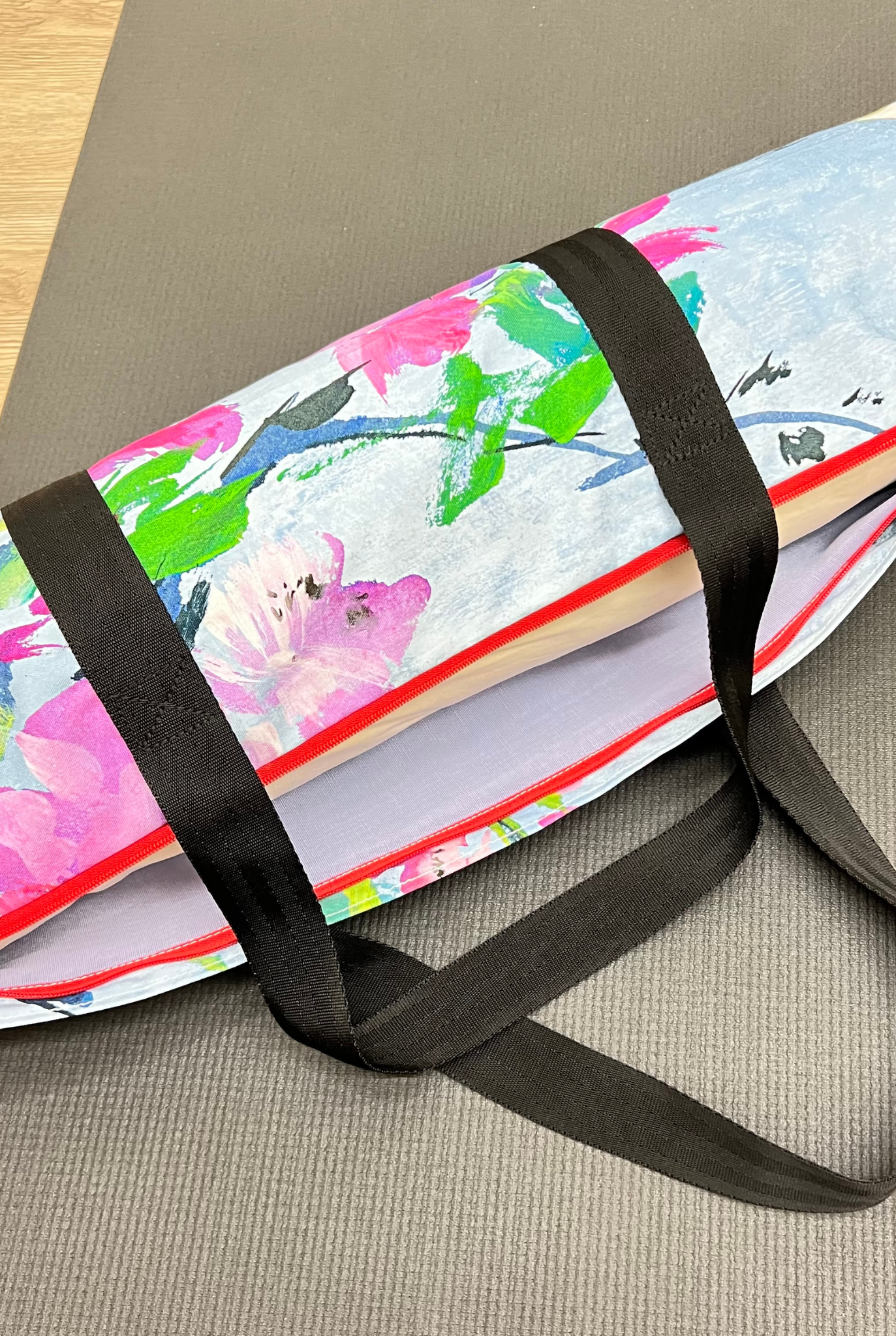 Colorful yoga mat with a black strap on a gray surface
