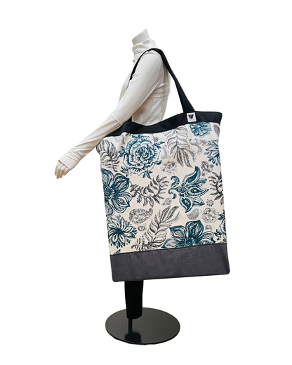 A large tote bag with a blue and gray floral pattern on a cream background, displayed on a white mannequin torso with a black stand against a white background.