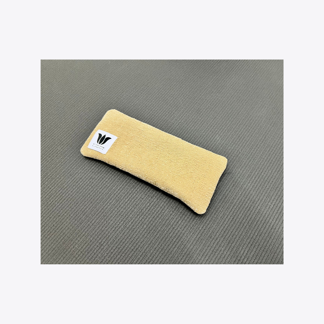 Beige eye pillow with a logo on a gray surface