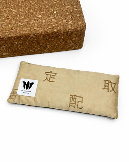 A gold fabric yoga eye bag with dark gold embroidered oriental characters and a white brand tag, shown next to a cork block on a white background.