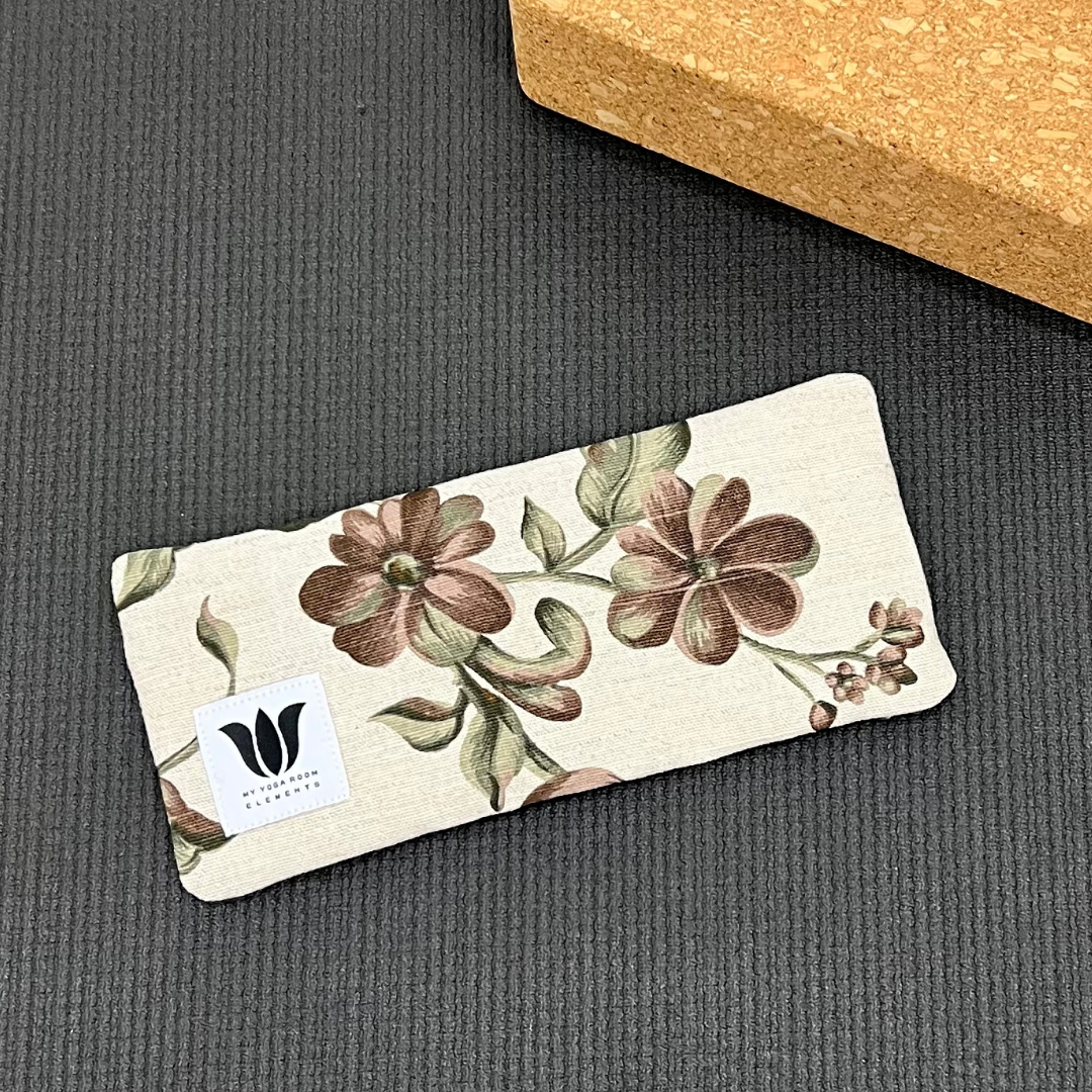 Floral design eye pillow on a textured gray yoga mat with a cork block.
