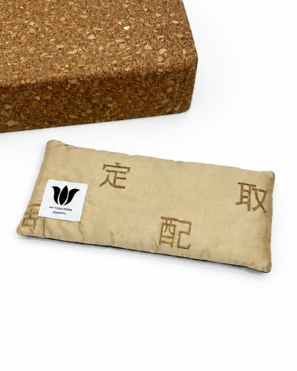 Gold embroidered silk eye pillow styled beside a cork yoga block; block not included